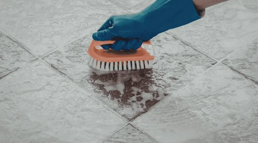 Close-up of a gloved technician scrubbing dirty grout lines on a tile floor in Chicago, deep cleaned by Carpet Cleaning Group